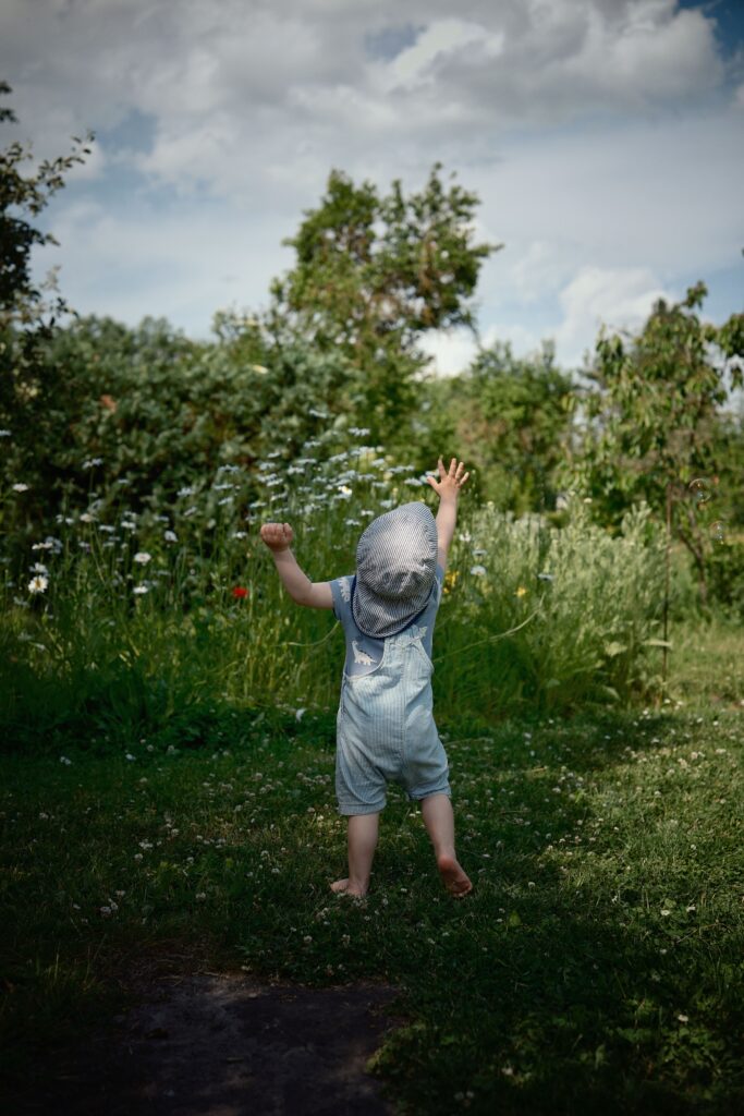 A young child enjoys a sunny day outdoors, surrounded by vibrant greenery and wildflowers.