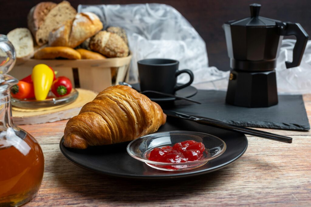 A cozy breakfast setup featuring a croissant, jam, and black coffee, creating a perfect morning scene.