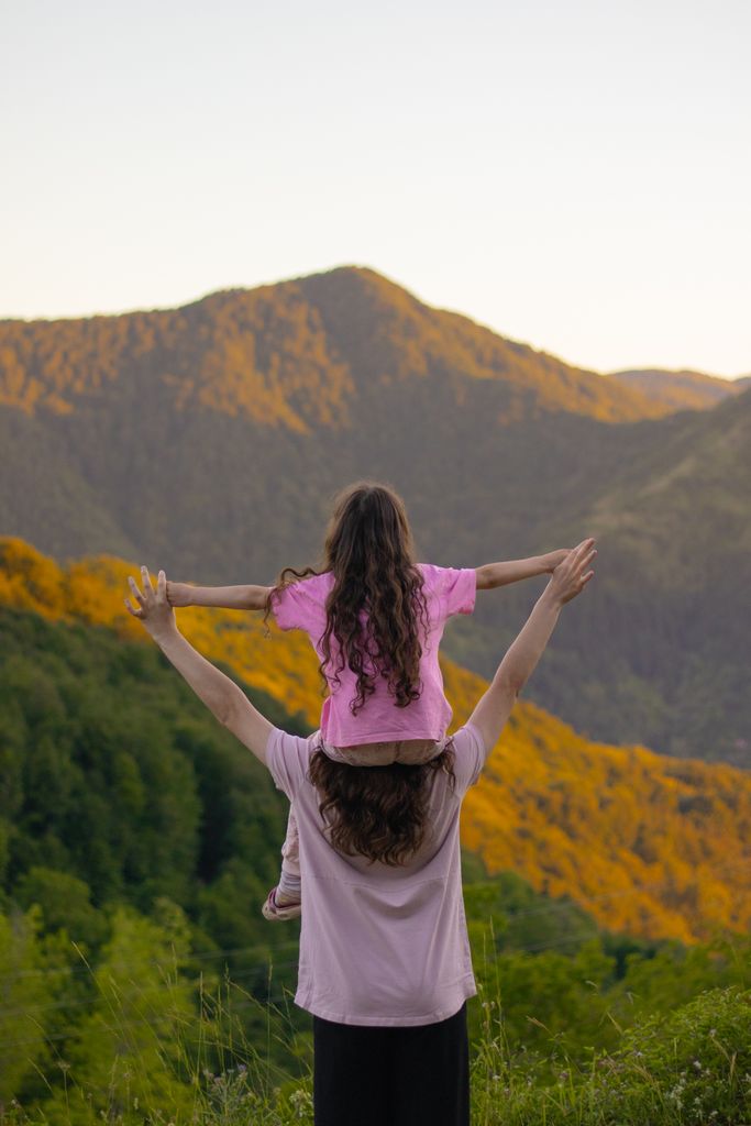 A mother and daughter celebrating nature atop a viewpoint with vibrant mountain scenery.