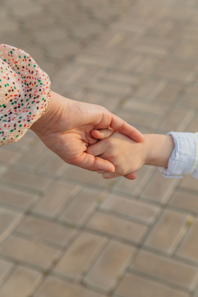 From above of anonymous mother and unrecognizable kid holding hands on street against blurred pavement in daylight in city outside