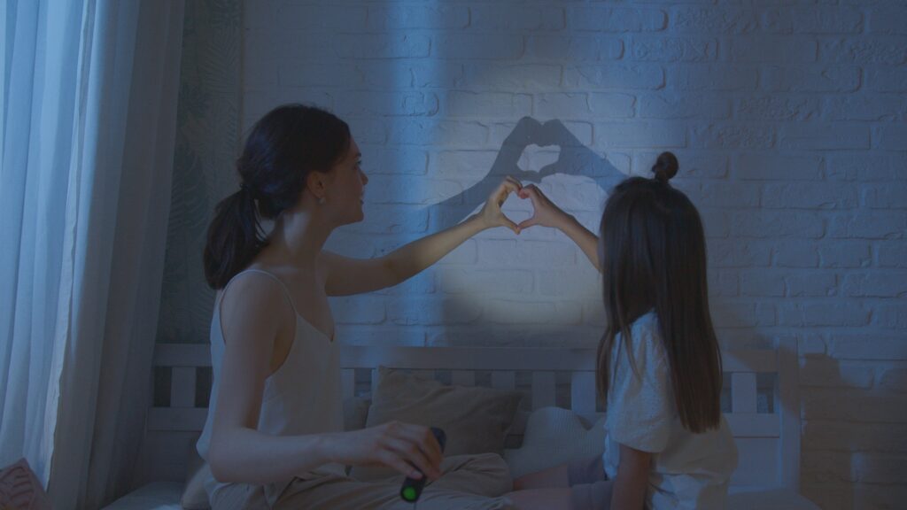 A touching moment of a mother and daughter forming a heart shape shadow together.