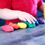 A young child with rainbow-colored modeling clay and stacking cups on a table indoors.