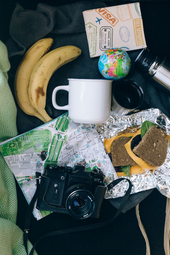 Flat lay of travel items including a map, camera, banana, and sandwich, perfect for adventure planning.